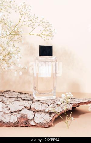 Perfume bottle with blank label on tree bark and white gypsophila flowers on neutral beige background. Front view Stock Photo