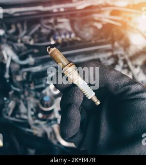 Automobile iridium spark plugs holds by auto mechanic hand with engine compartment blurred background and sunlight. Stock Photo