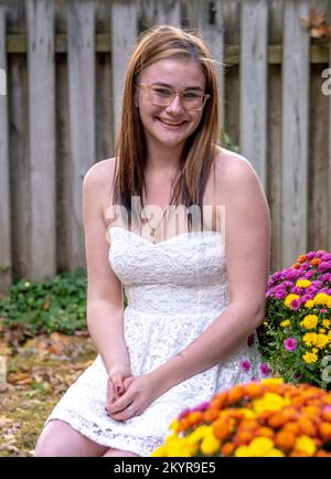 pretty young girl in a sleeveless white dress, poses in a garden with fall chrysanthemums Stock Photo