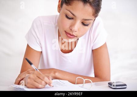 Keeping a dreamjournal. an attractive young woman lying in her bed writing something down in her diary. Stock Photo