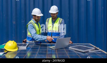 Shipment worker pointing at  shipping schedule on laptop computer, explain to colleague  about planning for next shipment. They use solar cell panel a Stock Photo