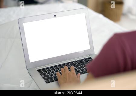 Back view of woman typing on laptop computer keyboard with white screen while sit relax on bed with white duvet. Close up. Work from home concept. Stock Photo