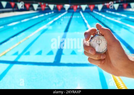 Time trials. a hand holding a stopwatch in front of a swimming pool. Stock Photo