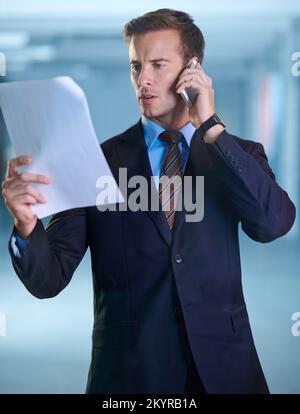 I have the paperwork in front of me...A young businessman reading a document while speaking on his cellphone. Stock Photo