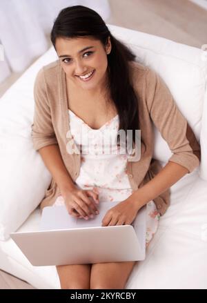 Keeping in touch through social networking. A young woman sitting on her sofa working on her laptop. Stock Photo