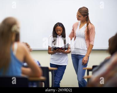 Best book report ever. a young student speaking in front of the classroom with her teacher standing next to her. Stock Photo