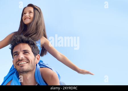 Spending quality time with my daughter. Low angle shot of a girl sitting on her fathers shoulders against a blue sky. Stock Photo