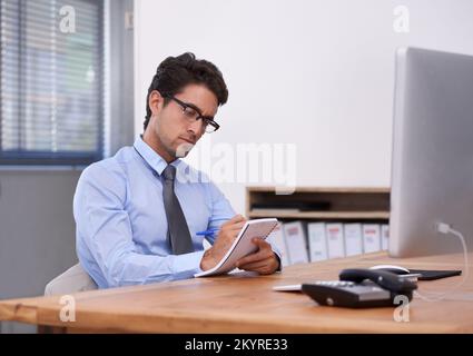 Writing down some great business ideas. Handsome young businessman writing down notes in his notebook. Stock Photo