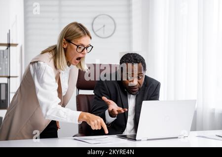 Angry female boss scolding African American office worker. A demanding manager-leader is annoyed by laziness and mistakes in the work of an employee Stock Photo