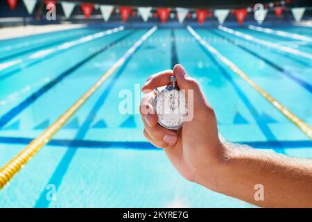 Time trials. Cropped shot a hand holding a stopwatch infront of a swimming pool. Stock Photo