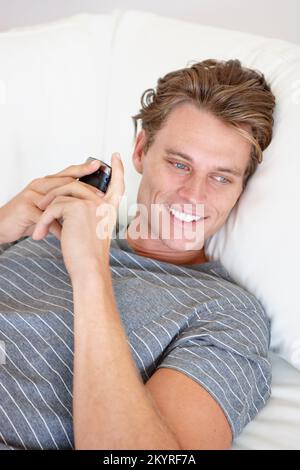 That text made my day...a handsome young man smiling and holding a phone while lying down. Stock Photo