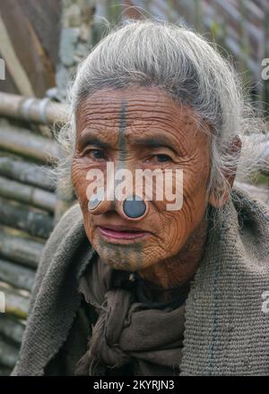 Ziro, Arunachal Pradesh, India - 03 04 2014 : Close up outdoors portrait of senior Apatani tribal woman with traditional facial tattoo and nose plugs Stock Photo