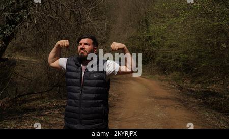 Middle-aged strong man raising his fists while exercising in the forest Stock Photo