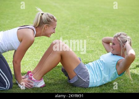 You can do just one more. A young woman doing crunches with the help of a trainer. Stock Photo