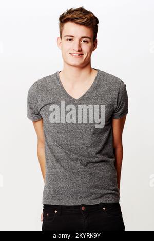Smiling bashfully. Studio shot of young man smiling while standing with hands behind his back. Stock Photo