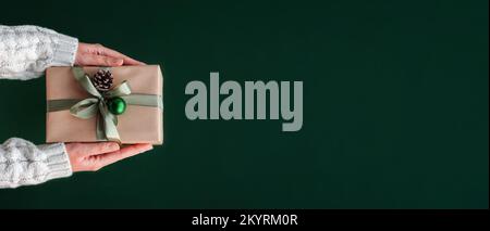 Female hands holding Christmas gift box on pastel green background. Stock Photo