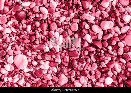 Trendy colorful small sea stone pebble background toned in Color of the year 2023 Viva Magenta. Red Pink abstract beach nature pattern color concept Stock Photo