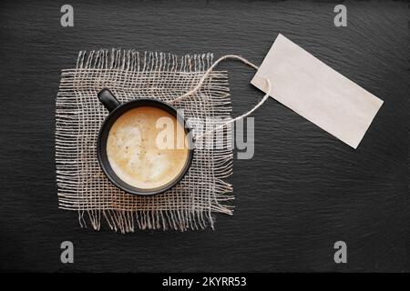 Coffee cup on rustic burlap and blank paper card. Top view with copyspace for your text. black background, cappuccino. price tag Stock Photo