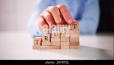Man's Hand Placing Last Alphabet Of Word Trust Over Wooden Block Stock Photo