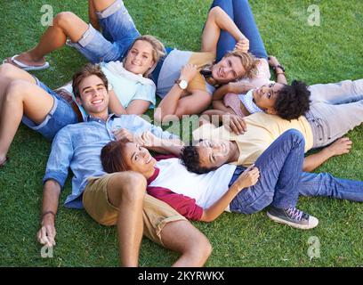 Theyre a close group of friends. High angle of a group of friends lying on their backs on the grass in a park. Stock Photo