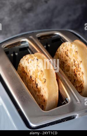 Toasted crumpets cooked in an electric toaster appliance.  On a dark stone background Stock Photo