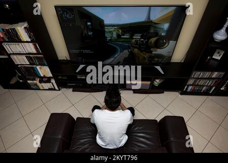 18 year old boy playing fighting video game on big tv screen Stock Photo
