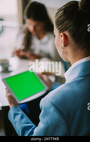 Bussinesswoman holding a tablet with a greenscreen in her hands and chatting with her collegues Stock Photo