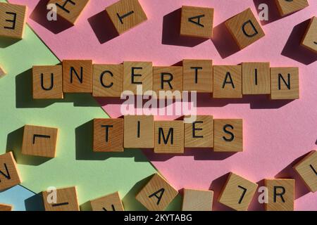 Uncertain Times, phrase surrounded by random wooden alphabet letters isolated on background Stock Photo