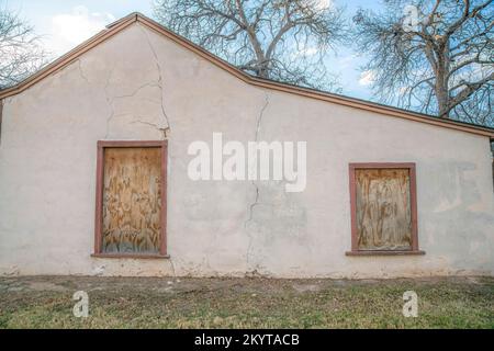 Abandoned building exterior with trees and sky background in San Antonio Texas. The old and weathered structure has a white cracked concrete wall and Stock Photo