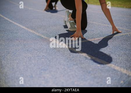 Female sportsperson is about to run on a blue sports track with her friend behind her Stock Photo