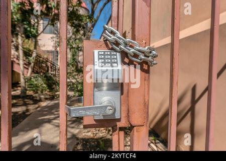 Austin, Texas- Gate with keypad lock of an apartment complex. Close up of a keypad lock on an iron railing gate against the view of trees and building Stock Photo