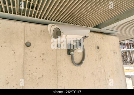 Austin, Texas- Close-up of a wall-mounted security camera. Close-up of a wall mount CCTV camera against the concrete wall and metal ceiling. Stock Photo