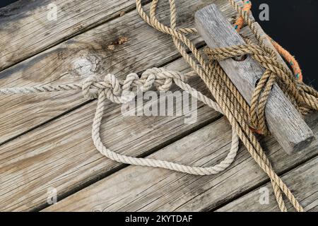 An old wooden jetty with ropes from boats attached to the mooring point, Stock Photo