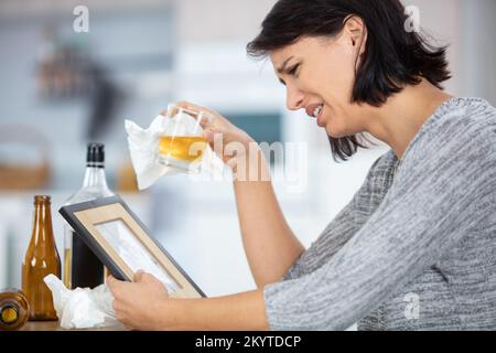 woman holding alcohol crying while looking at photograph frame Stock Photo