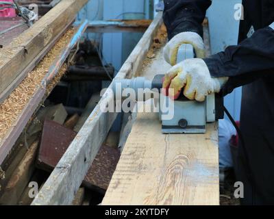 carpenter working with electric planer in the open workspace of the workshop, processing wooden material with the help of an electric planer Stock Photo
