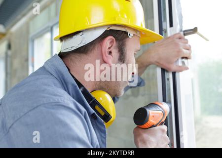 male builder using cordless drill on window Stock Photo