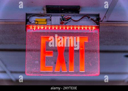 Red LED Exit ceiling-mounted sign- Lake Austin, Austin, Texas. Close-up of a modern exit sign illuminated by red LED lights on a ceiling. Stock Photo