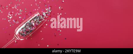 Champagne glass with star shaped sequins on a red background. Party, christmas, new year, celebration concept. banner. Top view. Flat lay. Stock Photo