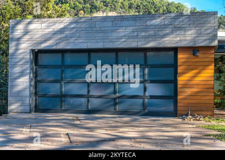 Modern detached garage exterior with frosted glass panels on garage door- Lake Austin, Austin, Texas. Garage exterior with gray concrete wall and wood Stock Photo