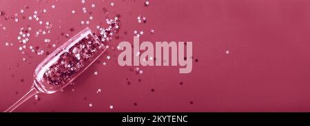 Champagne glass with star shaped sequins on a red background. Party, christmas, new year, celebration concept. banner. Top view. Flat lay. Stock Photo