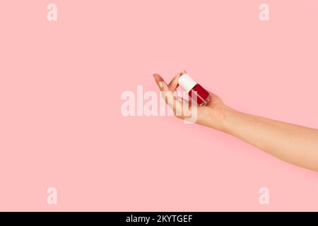 Woman hand holding a red nail polish bottle on a pink background with copy space Stock Photo