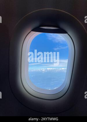 Looking out through the airplane window at the beautiful blue sky and sunlit white fluffy clouds. Smartphone photography Stock Photo