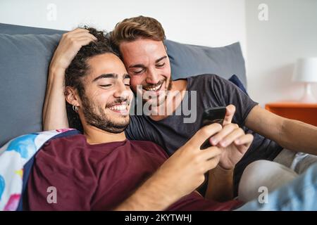 Affectionate gay couple watching content online with mobile cellphone in the bed - homosexual gay people stay together using smartphone - LFTB culture Stock Photo