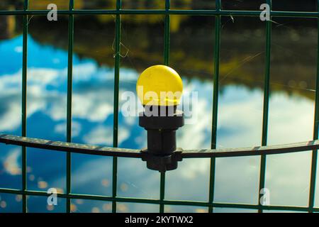 Yellow light bulb hanging near a fence reflecting sky and water in a tranquil setting Stock Photo