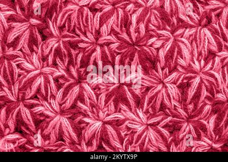 Trendy color of the year 2023. Texture of the knitted fabric toned in viva magenta color. Crochet from yarn, handmade. A pattern asterisks or snowflak Stock Photo