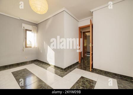 Empty room with two-color stoneware floors and mahogany-colored wooden doors and smooth walls painted gray Stock Photo