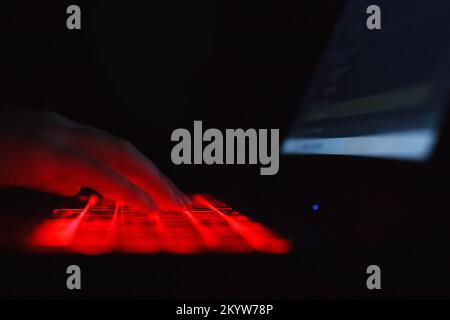 Person typing on laptop keyboard with red backlight Stock Photo