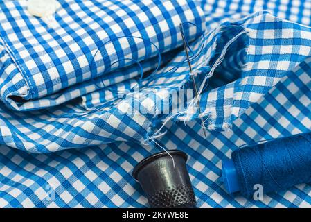 Needle and thread on a checkered fabric close-up. Seamstress or tailor's tools. Holes in clothes sew up with a needle Stock Photo