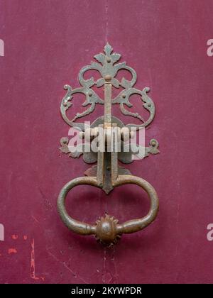 Closeup view of beautiful vintage brass door knocker isolated on ancient raspberry red wooden door, Montpellier, France Stock Photo