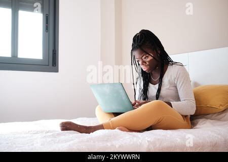 Black woman using netbook on bed at home Stock Photo